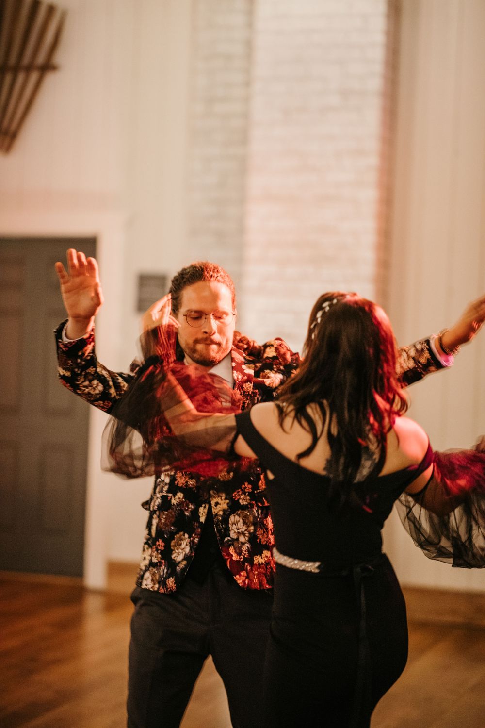 Couple performs an energetic dance in a floral jacket and black dress at a wedding reception.