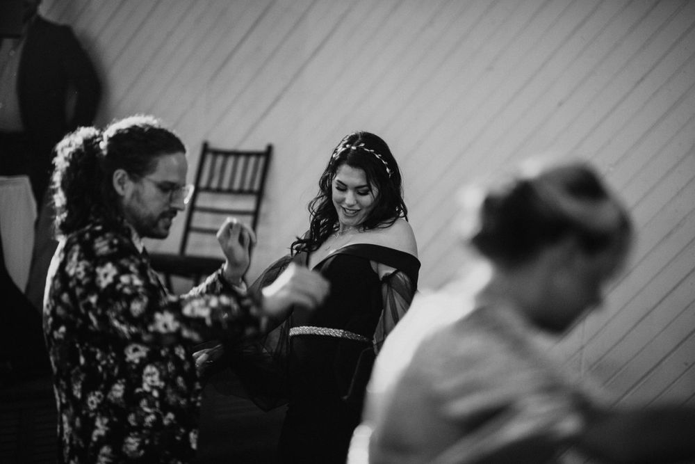 Black and white photo of a bride in an off-shoulder gown dancing joyfully with wedding guests.