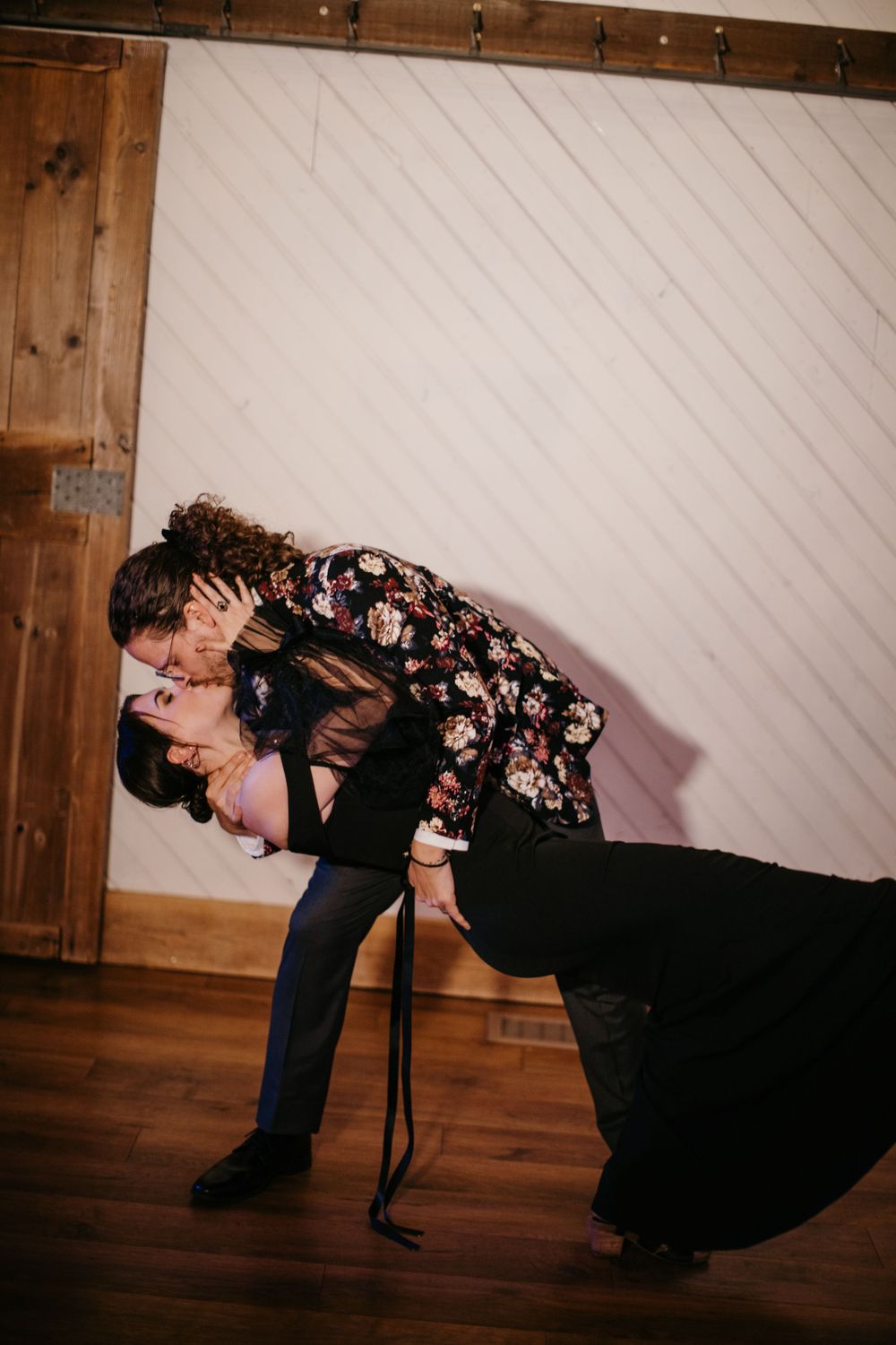 Couple sharing a romantic dip kiss on a wooden dance floor inside a rustic barn venue.