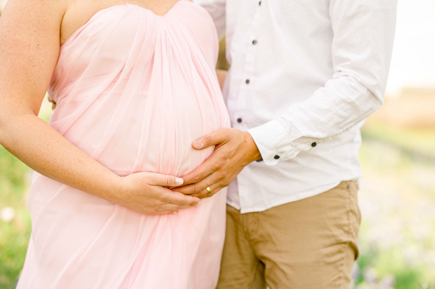 Maternity photography session outdoors with soft pink dress in natural lighting.