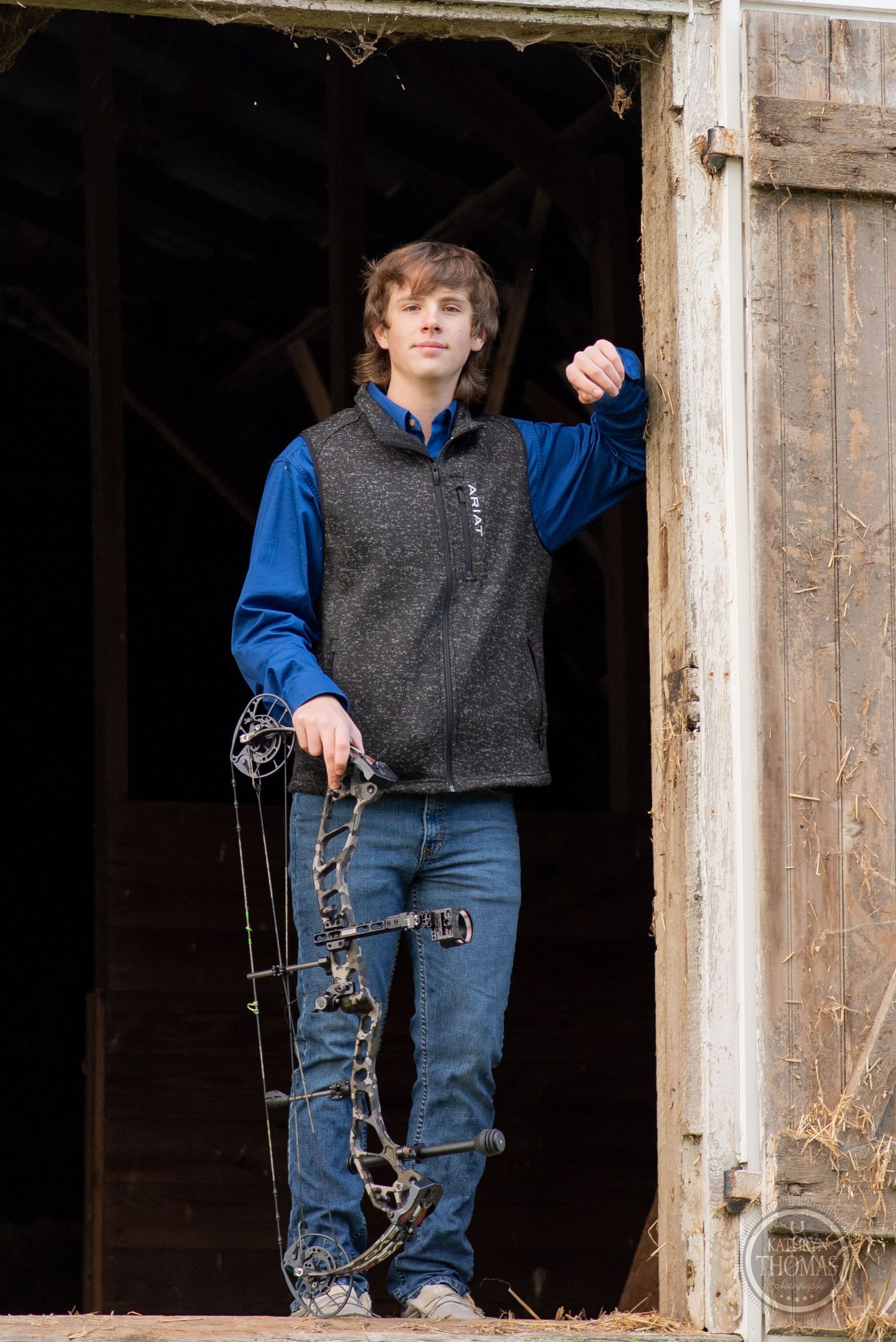 An archer stands in a rustic doorway holding archery equipment.
