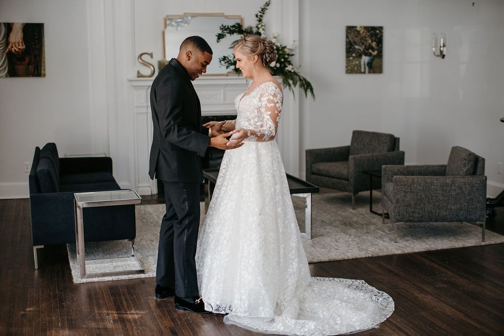 Groom reads wedding vows to bride in elegant lace long-sleeve gown during intimate indoor ceremony.