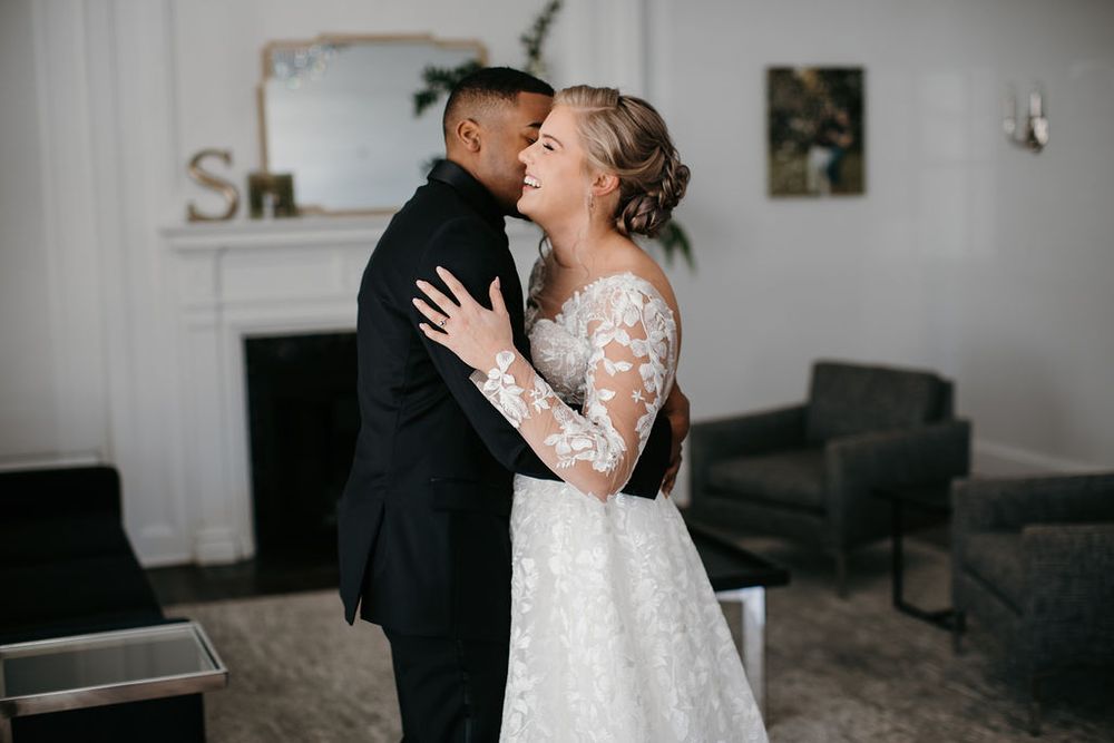 Bride and groom share a tender embrace in elegant wedding attire during indoor first look moment.