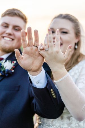 Close-up of hands showing off wedding rings against a blurred background.