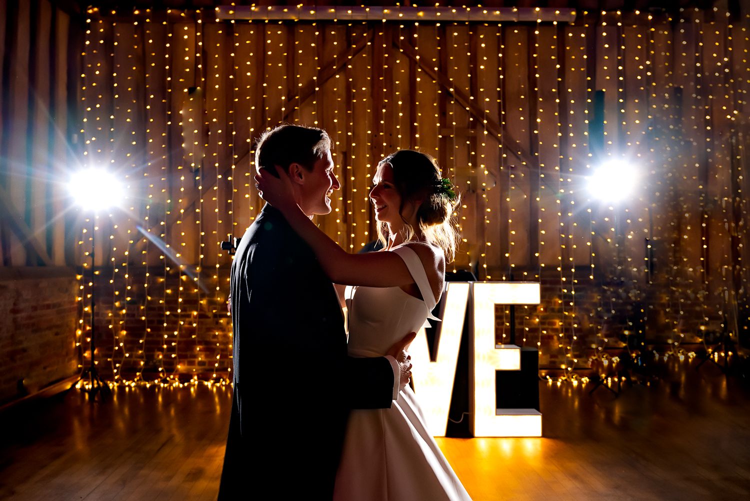 A romantic first dance moment with twinkle lights and illuminated LOVE sign in the background.