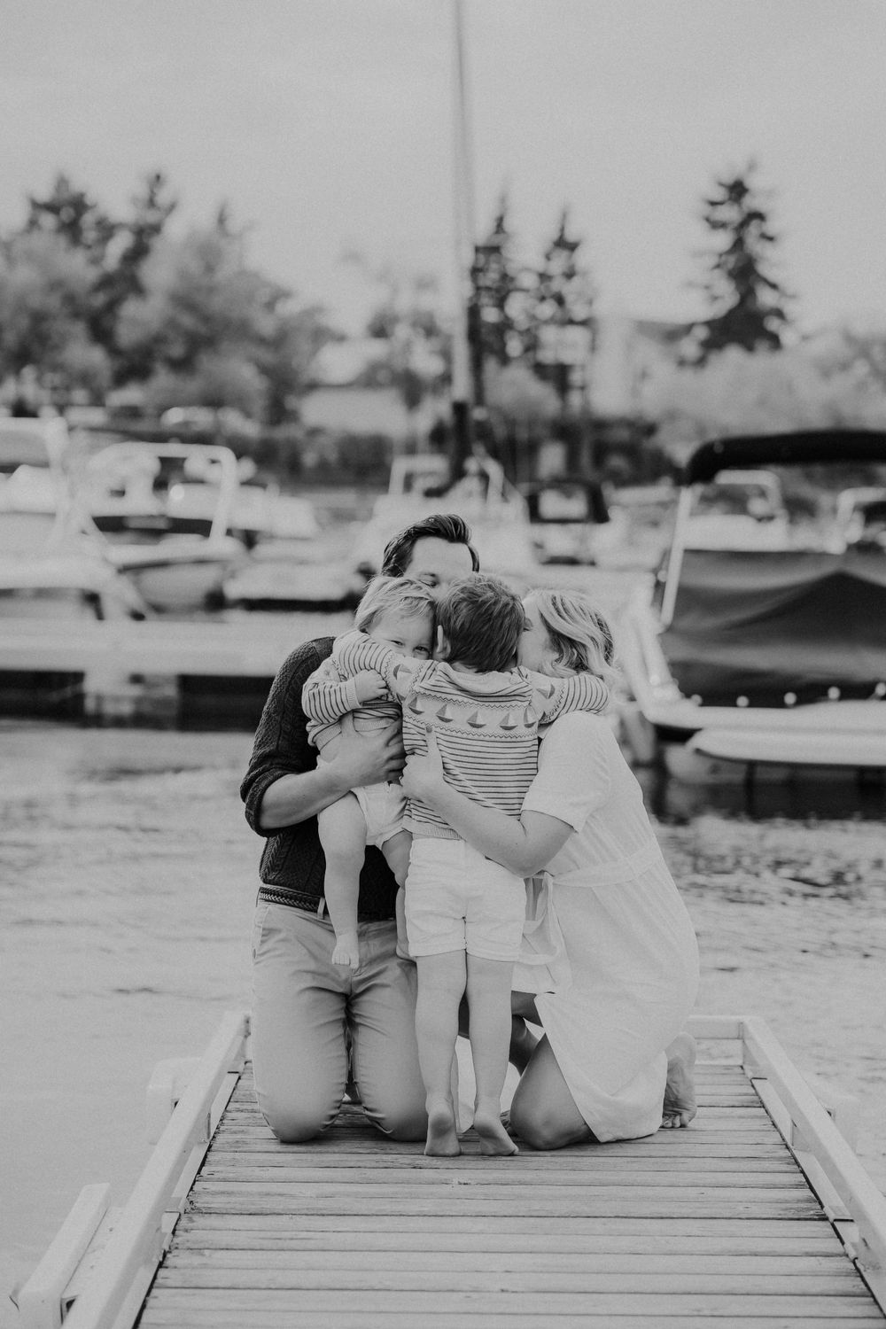 Black and white photo of a family sitting together on a wooden dock during a casual outdoor photoshoot.