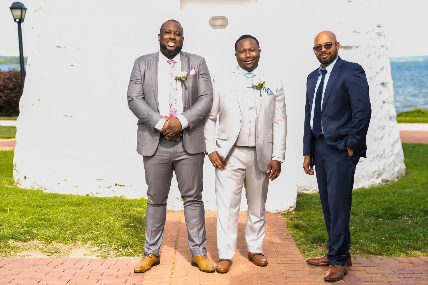 Three men in formal suits pose together in front of a white lighthouse.