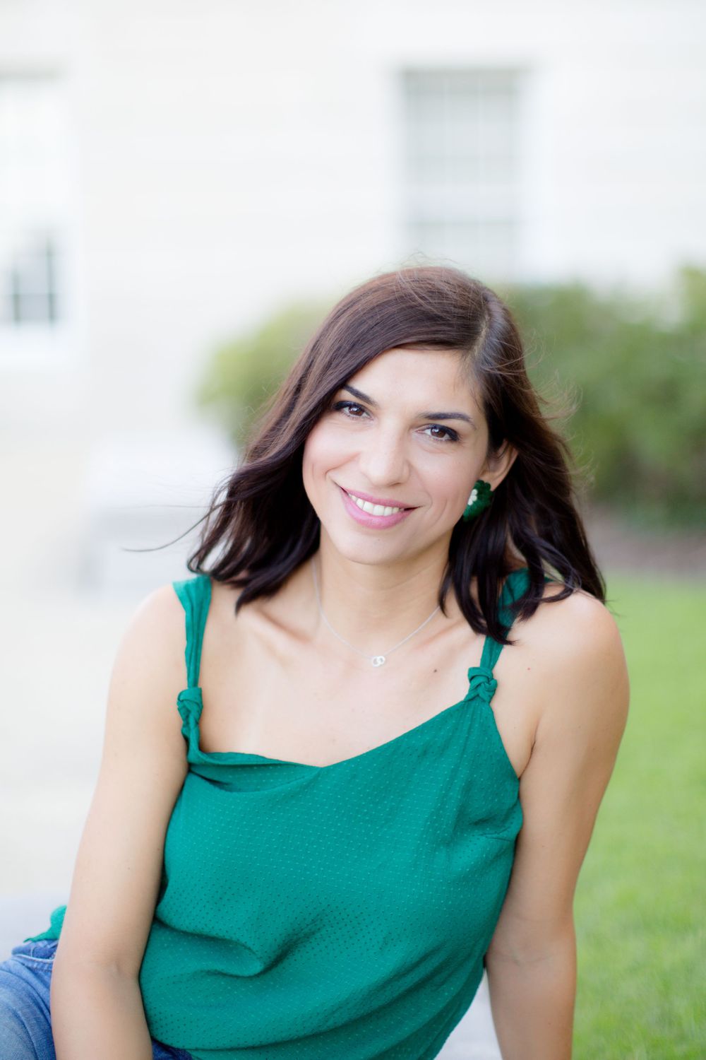 Woman in green tank top smiling outdoors on sunny day.