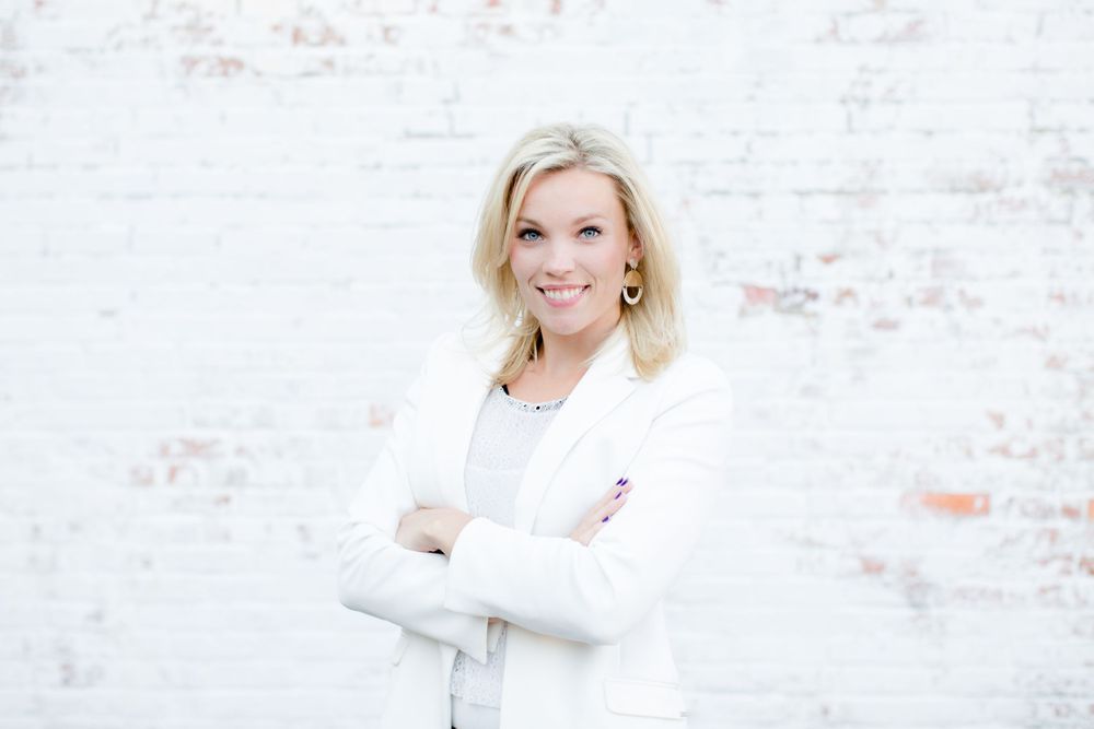 Professional portrait of woman in white blazer with arms crossed.