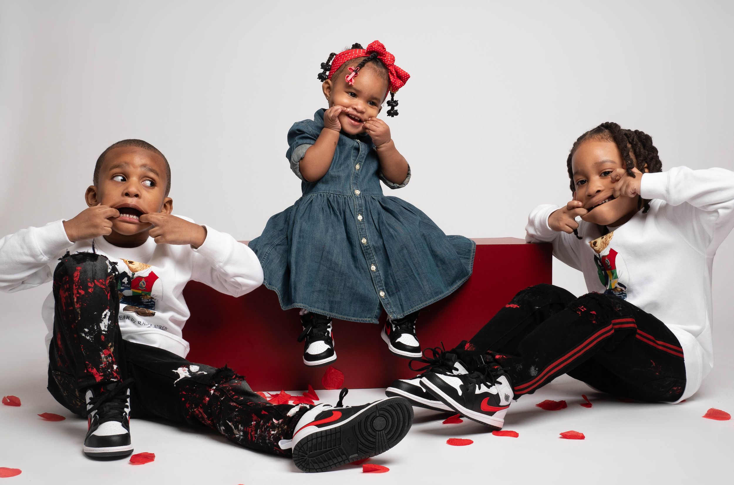 Three children in casual wear posing playfully on red furniture.