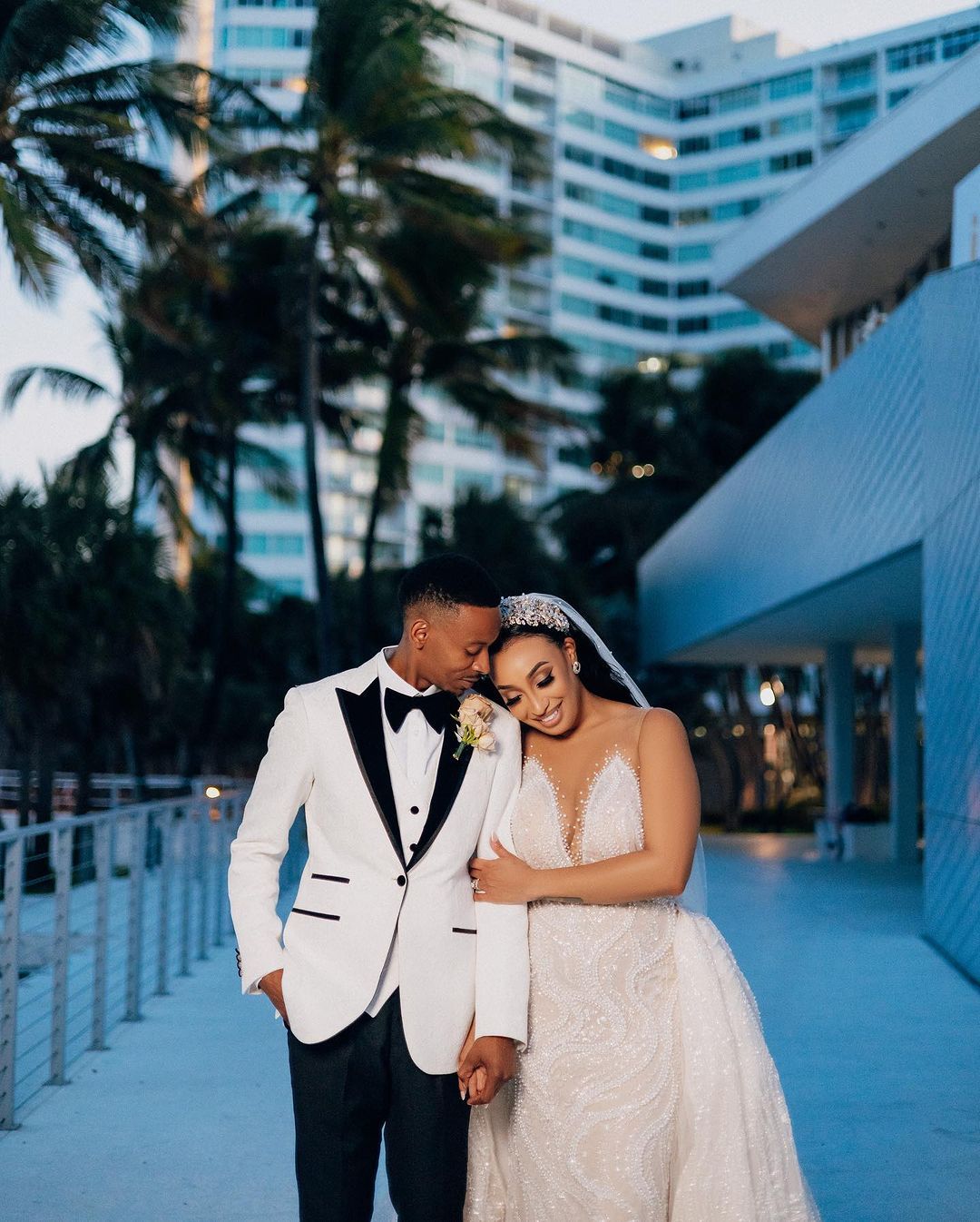 Newlywed couple sharing an intimate moment at dusk outside a modern hotel with palm trees swaying in Miami.
