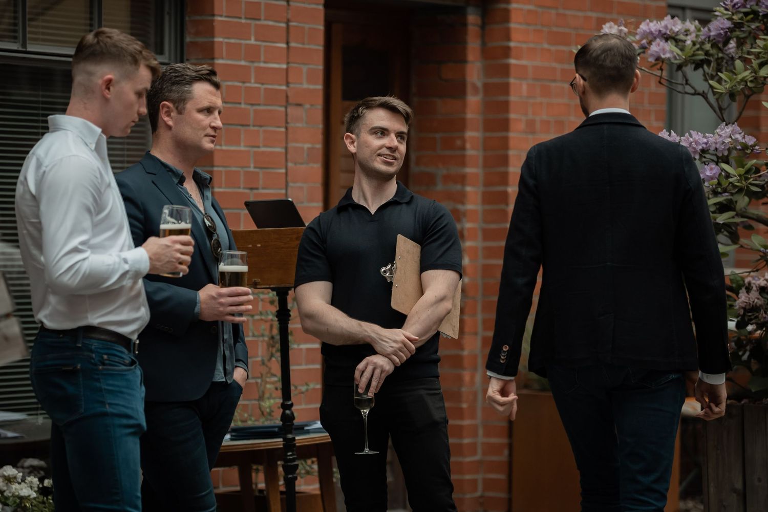 A small group of professionals having drinks and conversation outside a brick building.