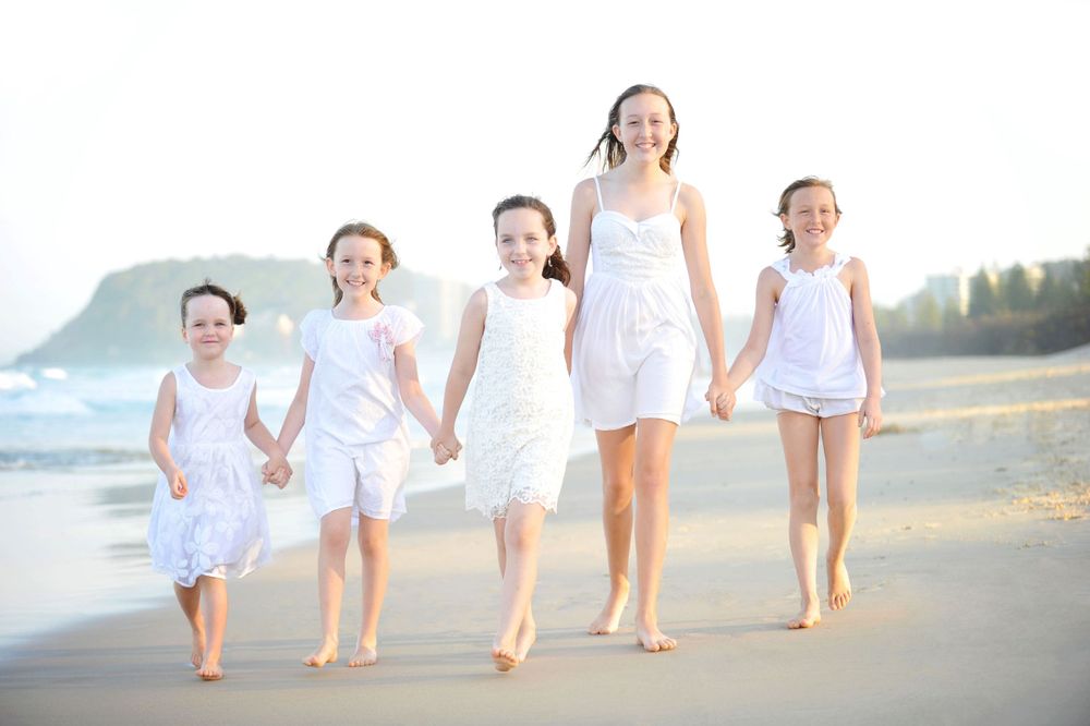 5 Girls wearing white walking along beach holding hands