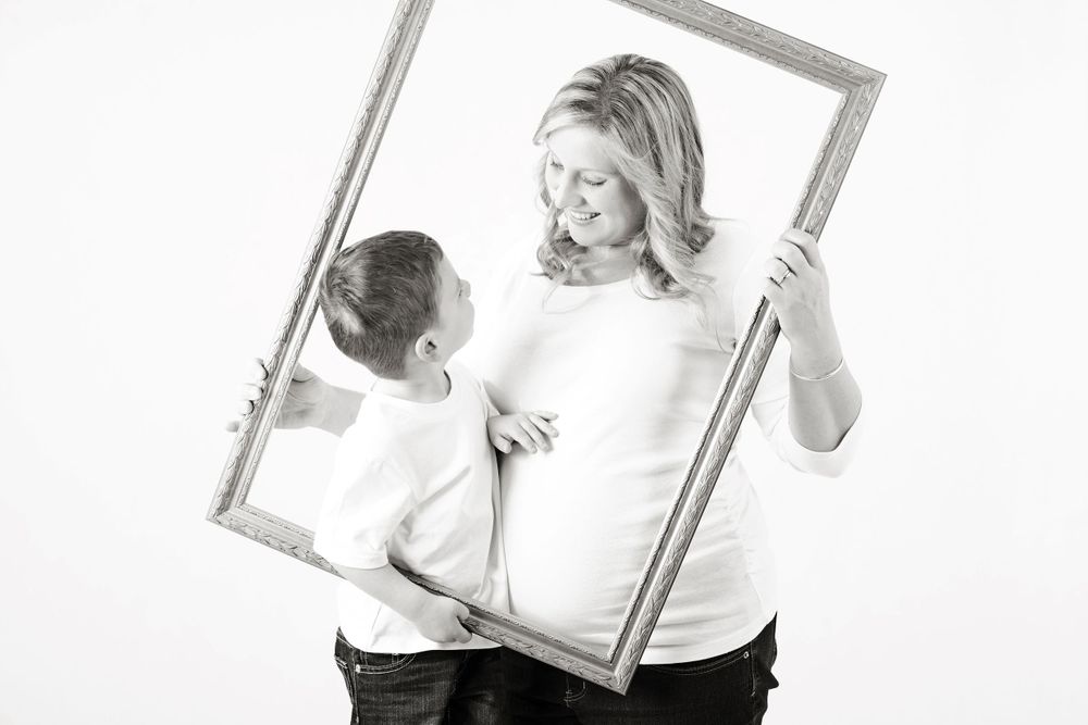 Pregnant mum smiling at toddler through photo frame