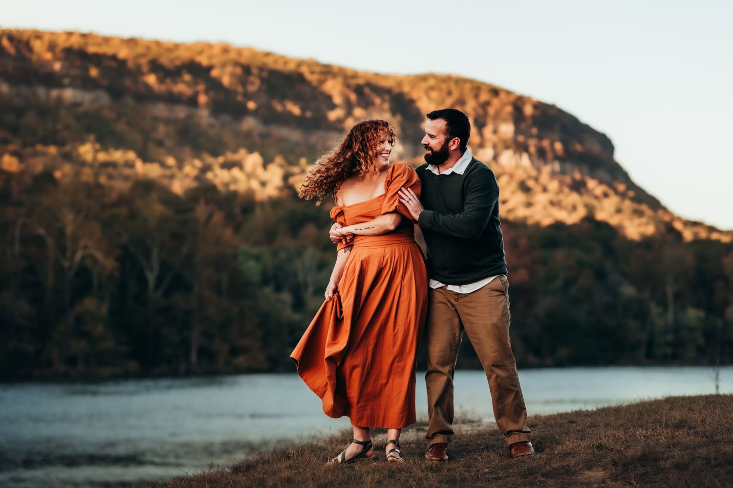 husband and wife dance by the river with a mountain view behind them at autumn in Chattanooga