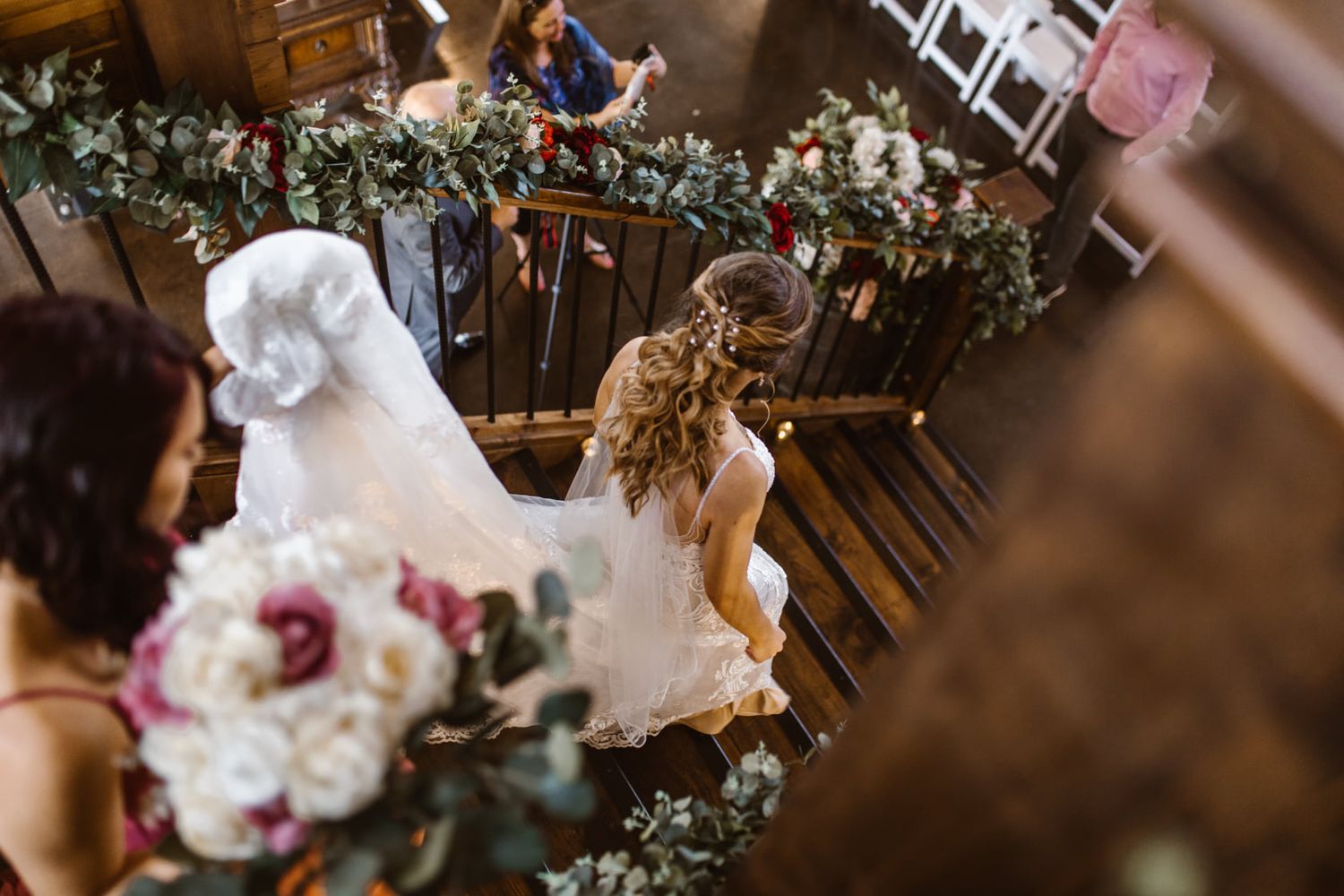 Wedding dress and floral arrangements cascade down wooden staircase decorated with greenery.
