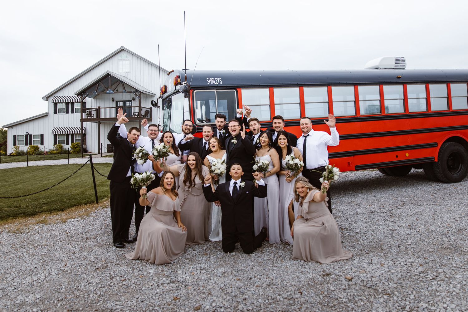 Wedding party poses together in front of a retro red school bus at a rustic venue.