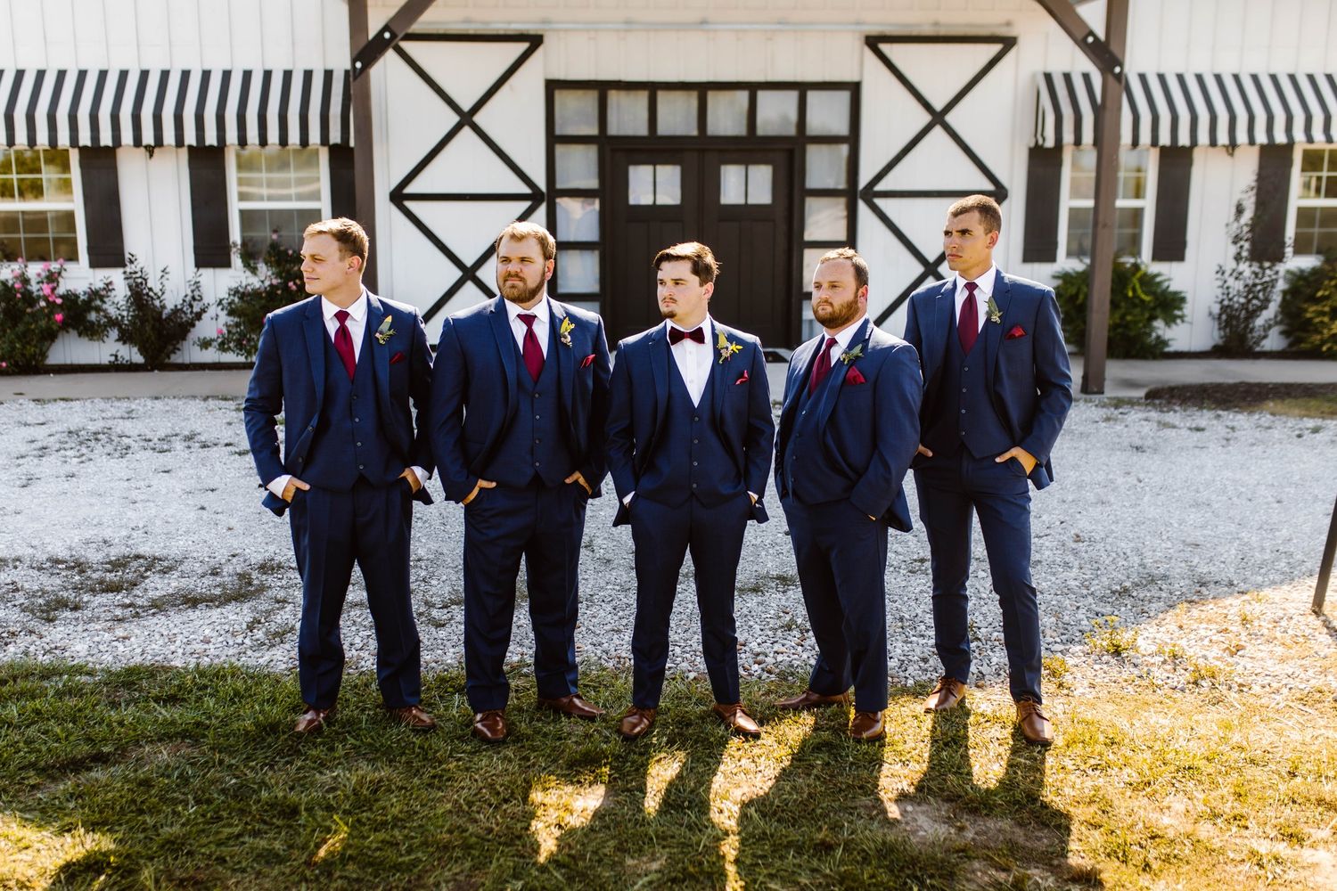 Groomsmen in navy suits and bow ties pose confidently outside venue entrance.
