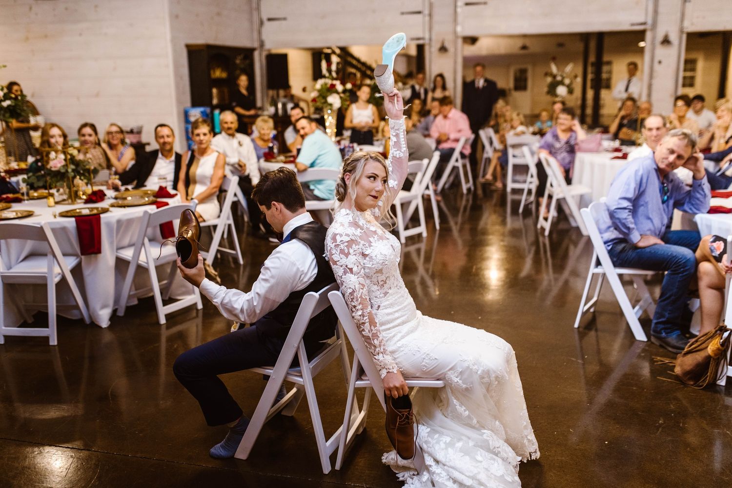 Wedding couple participates in reception game on white folding chairs.