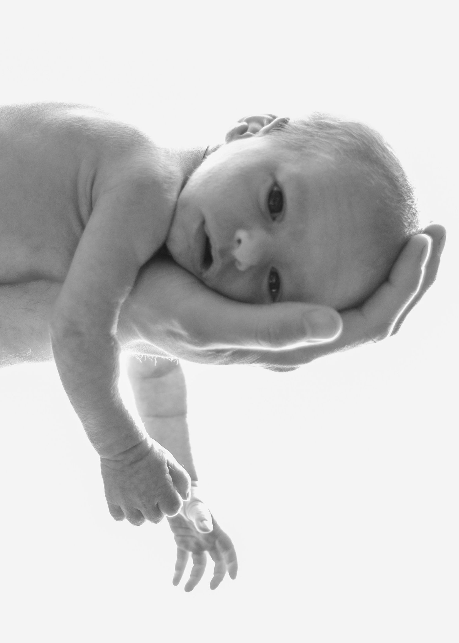 Black and white portrait of baby resting on supportive hands.