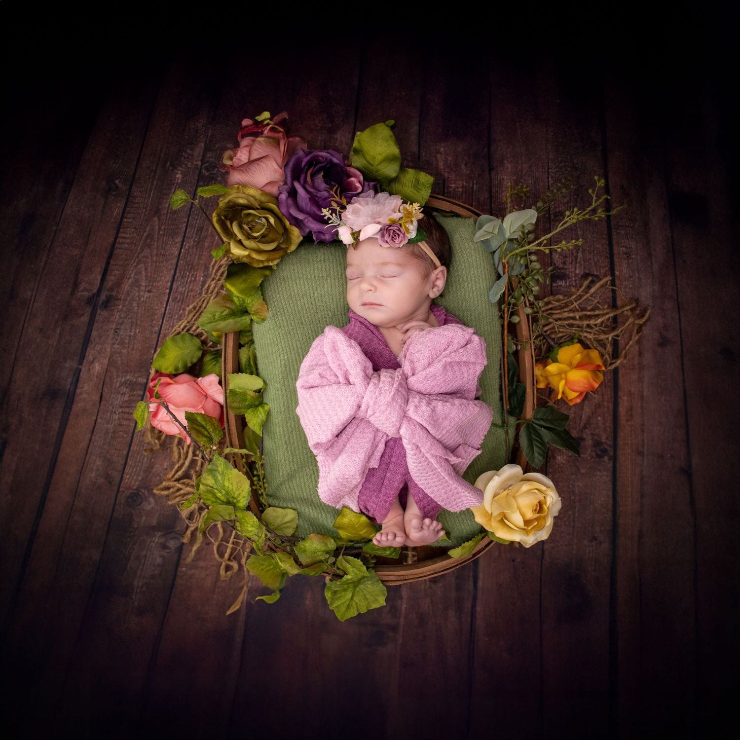 Overhead shot of sleeping infant in pink wrap surrounded by floral wreath.