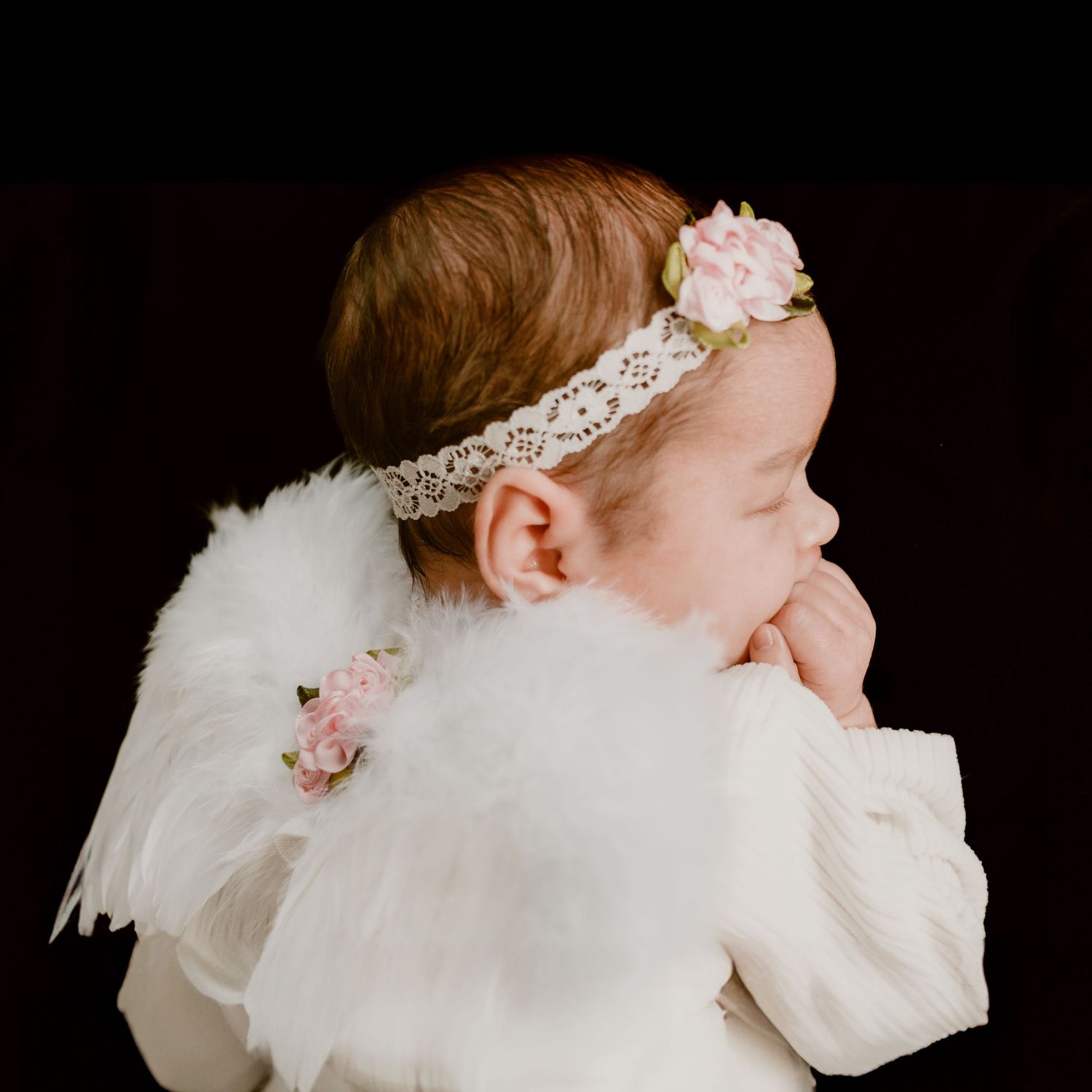 Side profile of baby wearing white lace headband and angel wings.