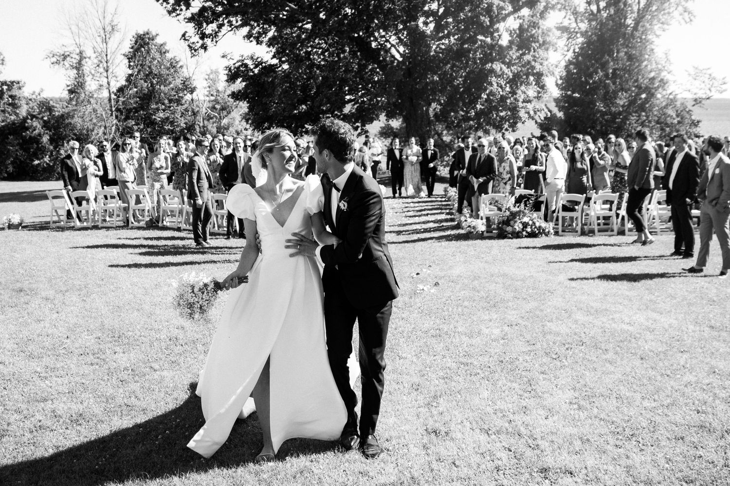 Black and white photo of a bride and groom walking together after an outdoor wedding ceremony.