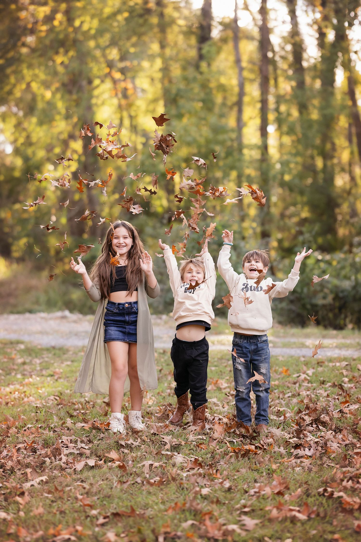 Three joyful children playing with autumn leaves in a forest, capturing the essence of fall in an outdoor photoshoot