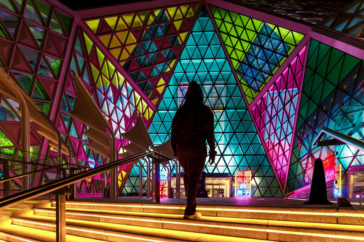 Colorful geometric architecture with stained glass patterns creates a vibrant corridor with silhouettes.