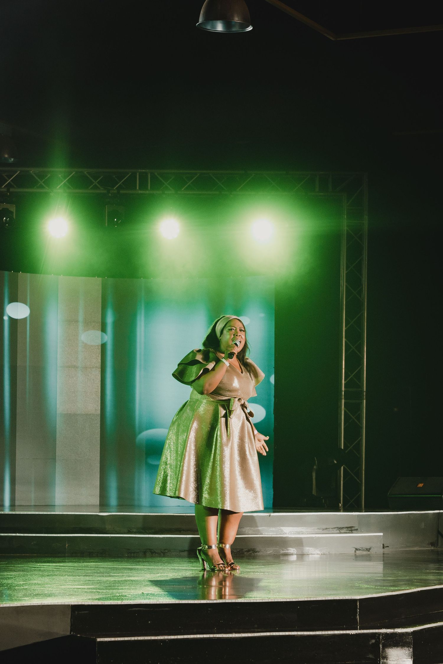Stage performance with green lighting featuring performer in shimmering dress.