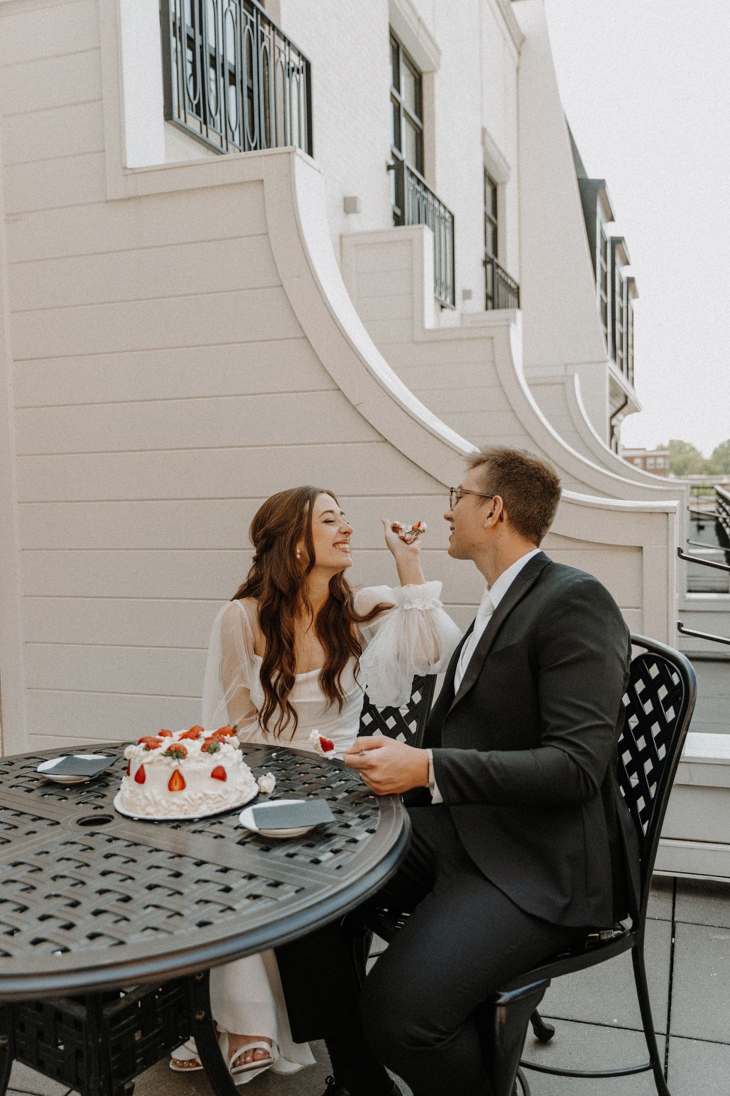 Couple shares dessert and laughter at outdoor cafe table.