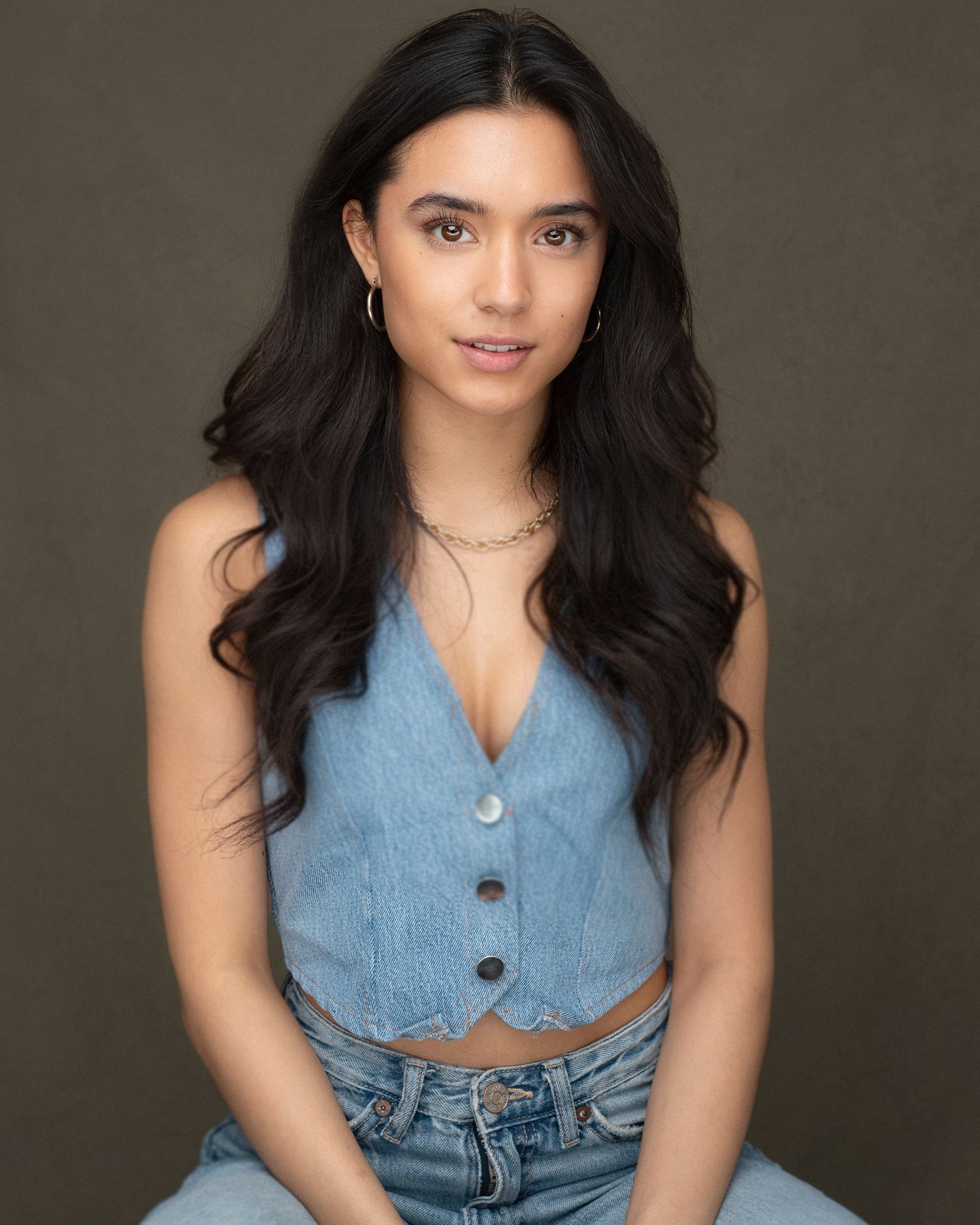 Fashion portrait in denim crop top and jeans with long dark hair against dark background.