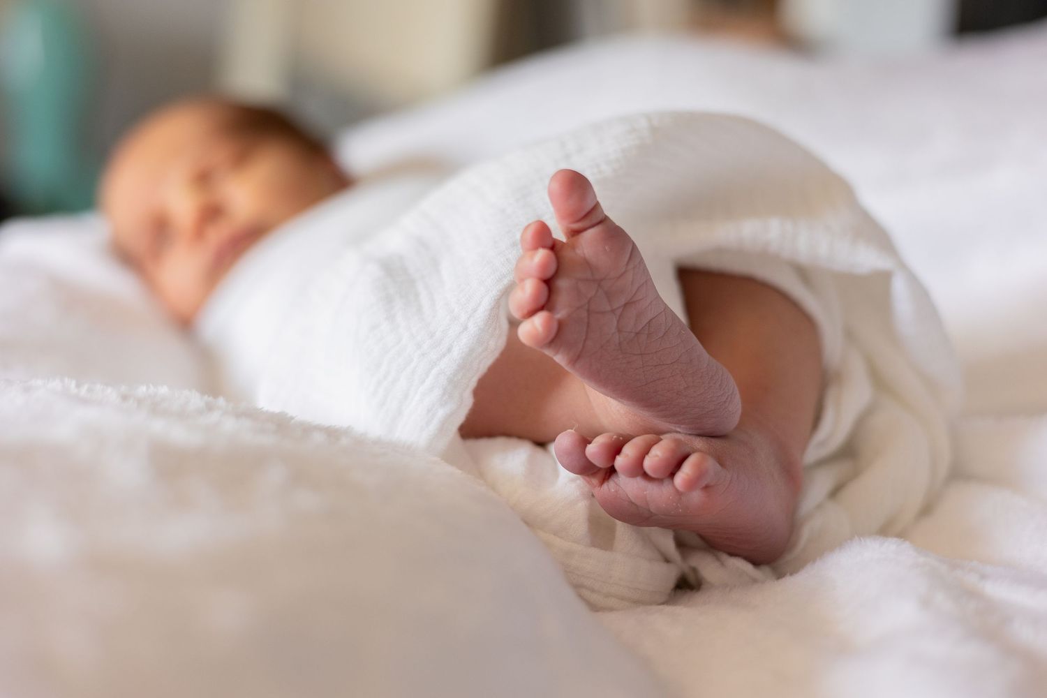 A tiny baby's feet peek out from white blankets while sleeping peacefully in bed.