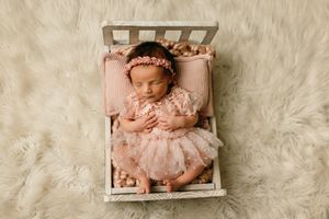 Baby wearing pink lace outfit resting on white fur backdrop during newborn photoshoot.