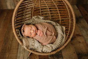 Sleeping newborn nestled in round woven basket on wooden floor.