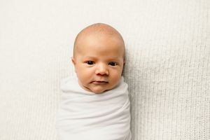 Progression of newborn expressions while wrapped in white swaddle.