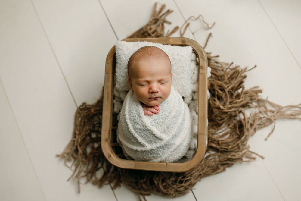Newborn photography series showing baby wrapped in white fabric against rustic wooden backgrounds.