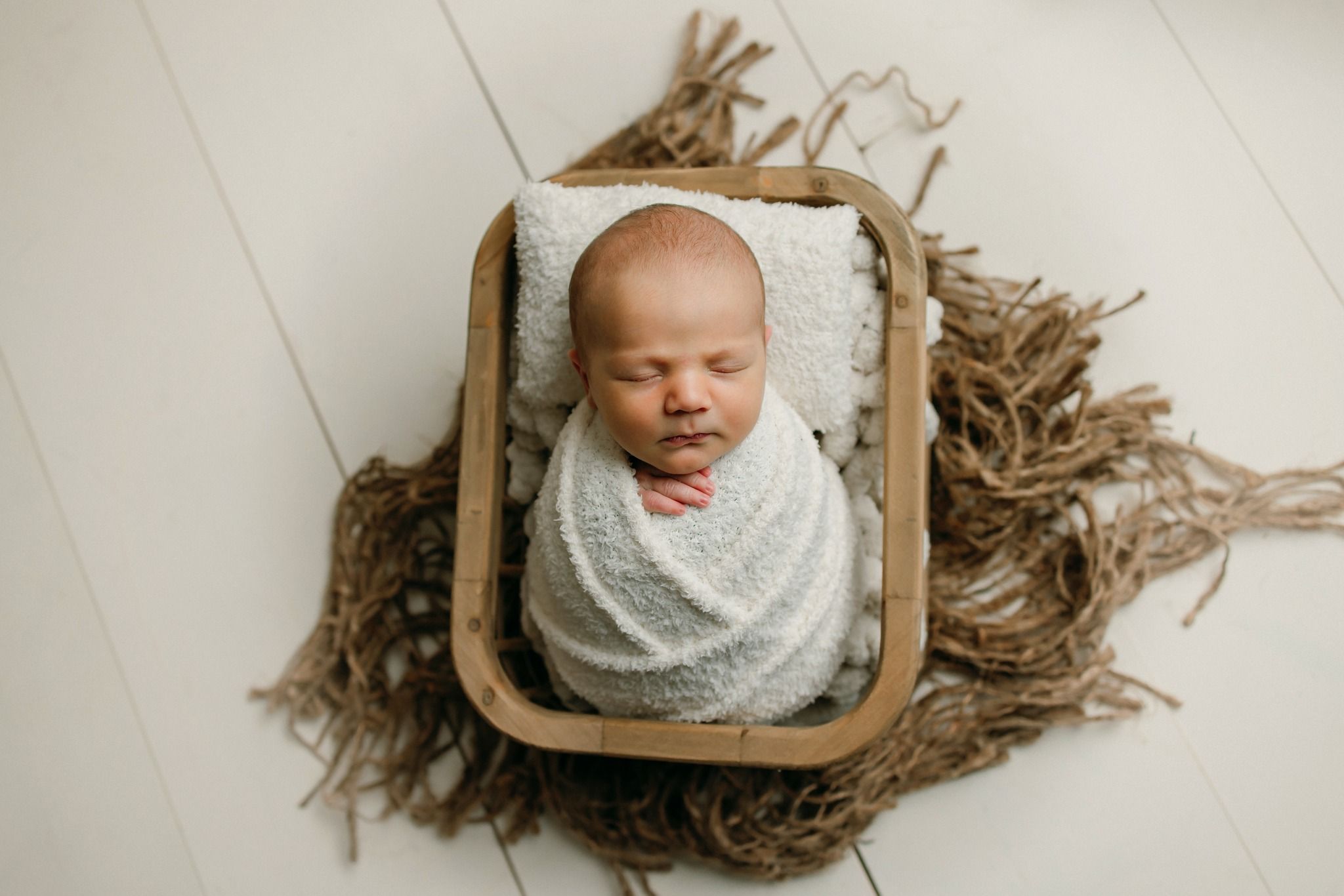 Newborn photography series showing baby wrapped in white fabric against rustic wooden backgrounds.