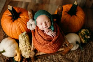 Autumn themed newborn photo with baby nestled among orange pumpkins and fall decorations.