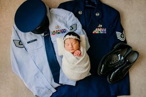 Newborn baby sleeping surrounded by military service uniform in styled photo.