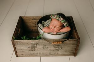 Sleeping newborn posed in rustic wooden crate wearing a floral crown.