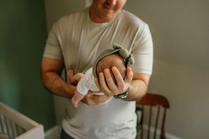 Close-up of hands holding and swaddling a sleeping newborn baby.