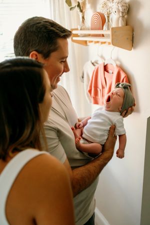 Parents sharing joyful moment with baby in nursery with decorated shelves.