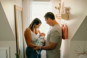 Parents holding newborn baby together in soft natural light by nursery window.