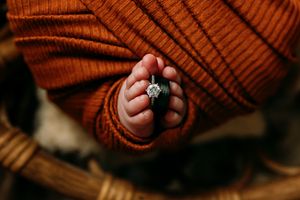 Close-up of newborn feet with ring against rust-colored knit fabric texture.