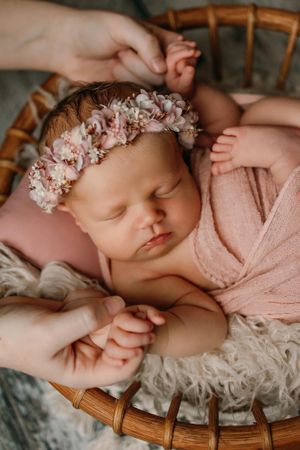 Newborn baby wrapped in pink fabric lying on soft white fur with delicate floral headpiece.