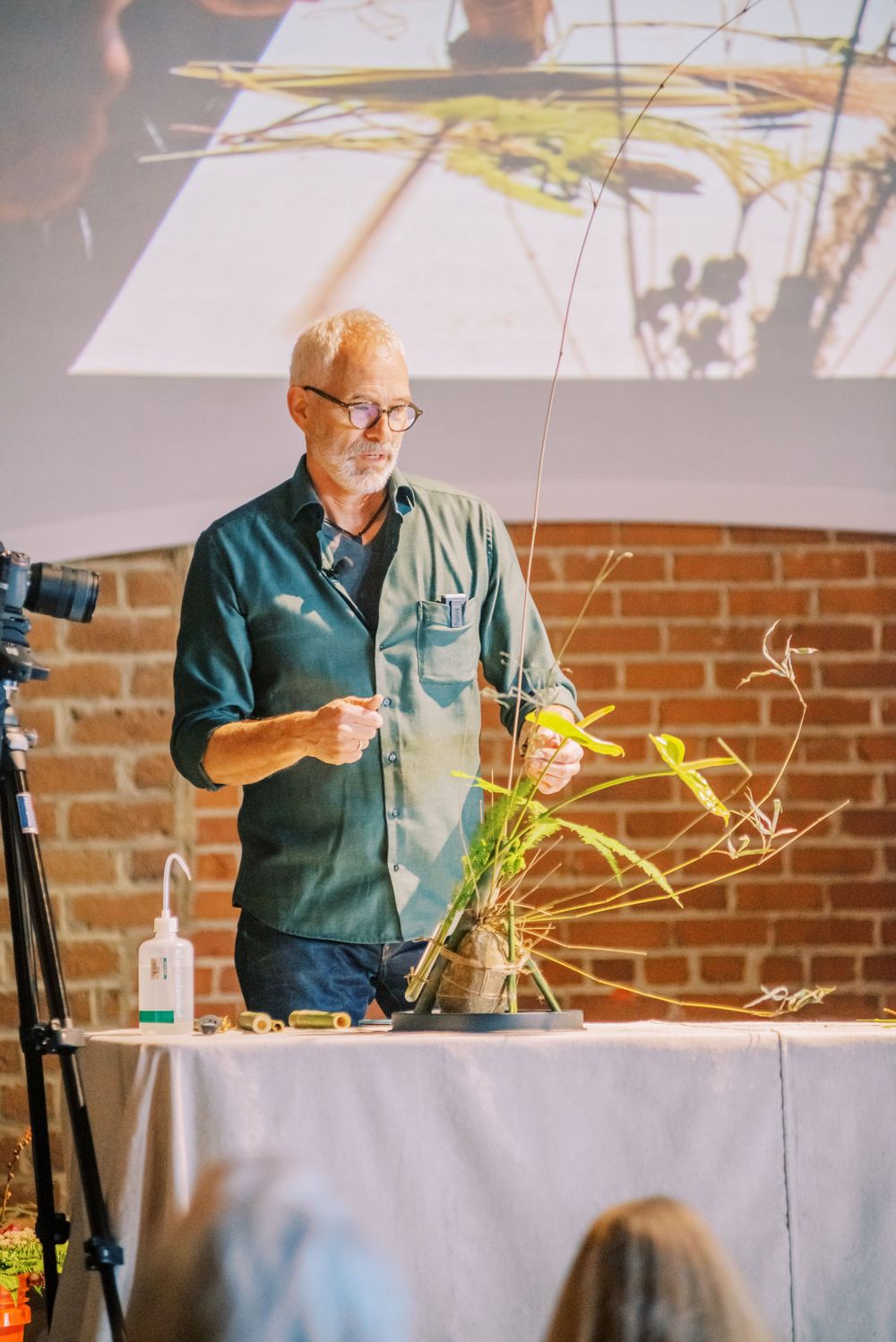 Presenter giving demonstration at podium with projection screen in brick-walled venue.