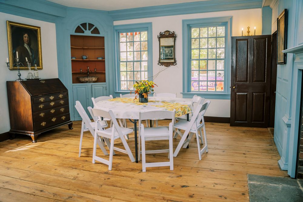 A bright blue dining room with wood floors, white chairs and round table.