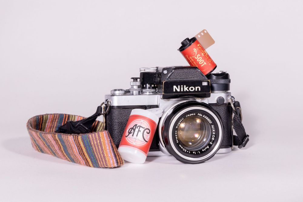 Vintage Nikon film camera with a colorful striped strap and two film canisters.