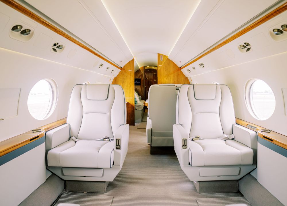Interior view of a private jet cabin showing plush white leather seats and wood trim details.